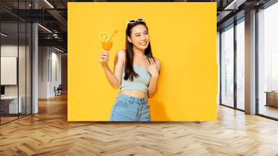 Summer portrait of pretty Asian girl with orange juice drink in isolated yellow color studio background Wall mural