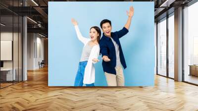 Surprised Asian couple standing back to back smiling and opening hands in light blue isolated studio background Wall mural