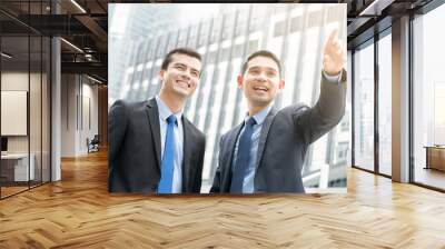 Two businessmen standing outdoors in the city with one hand poin Wall mural