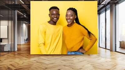 Waist up portrait of positive African couple smiling in isolated yellow color studio background Wall mural