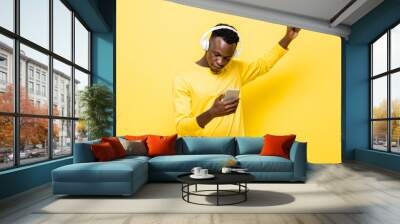 young african man in casual attire wearing wireless headphones listening to music with mobile phone  Wall mural