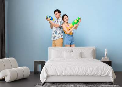 Young Asian couple in summer outfits with water guns in studio blue background for Songkran festival in Thailand and southeast Asia Wall mural