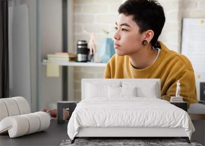 Young Asian tomboy woman in casual attire working from home on laptop computer in living room Wall mural