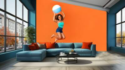 Young energetic African American woman holding beach ball and jumping Wall mural