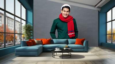 Young handsome Asian man wearing colorful red and green Christmas attire posing in studio with hands in pocket Wall mural