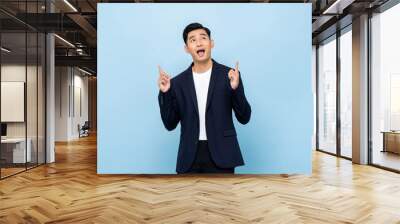 Young handsome southeast Asian businessman pointing hands and looking upward on light blue studio background Wall mural