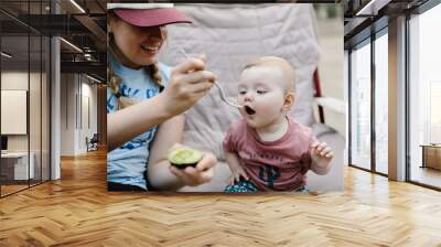 mom feeding her baby daughter an avocado outdoors while camping Wall mural