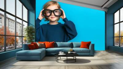 curious little girl wearing oversized glasses looking up on a blue background - adorable child with big eyes and playful expression Wall mural