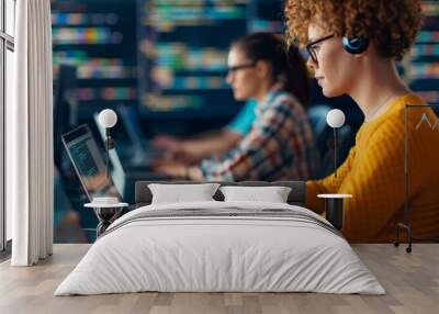 focused female programmer working on laptop in modern office with blurred background of another coder - coding project team collaboration concept Wall mural