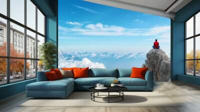 man sitting in meditation on mountain peak overlooking majestic snowy mountain range. Wall mural