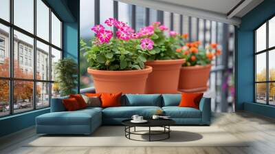 vibrant pink and orange flowers in terracotta pots on balcony railing with city skyline in background. Wall mural