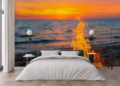 warm bonfire flames burning bright against a stunning sunset on a sandy beach at dusk. Wall mural