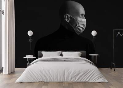 Coronavirus, Bio Protection Concept. Close up profile portrait of handsome bald man wearing medical mask, black turtleneck and praying. Copy-space. Studio shot Wall mural