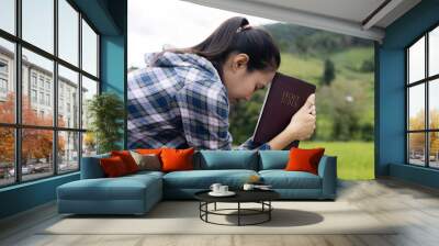 Woman praying on holy scripture in field during beautiful sunris Wall mural