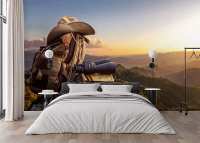 Binocular with map paper and hiker hat and backpack on top of rock mountain at sunset Wall mural