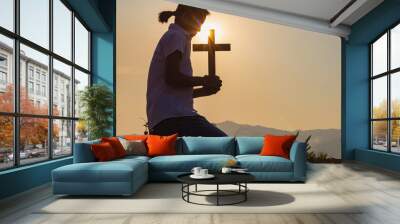 Christian, Christianity, Religion copy space background. Human kneeling down praying and holding christian cross for worshipping God at sunset background. Wall mural