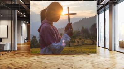 Christian young woman praying with a cross at sunset sky background, Christian Religion concept background. Wall mural