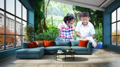 Cute asian little boy and girl reading book sitting in garden Wall mural