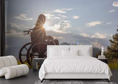 Disabled handicapped woman is sitting on wheelchair at sunset. Wall mural