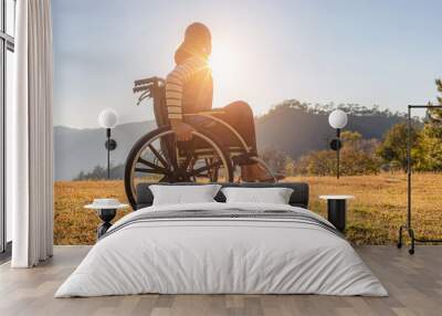 Disabled handicapped woman is sitting on wheelchair at sunset. Wall mural