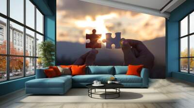 hands holding piece of jigsaw puzzle and sunset background. teamwork concept Wall mural