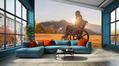 Person sitting on wheelchair looking sunset on mountain park.. Wall mural