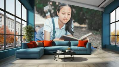 pretty teenage girl lies on meadow thinking and reading book over garden background. Wall mural