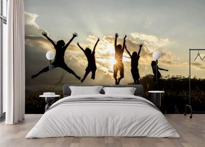 Silhouette group of happy children jumping playing on mountain at sunset, summer time Wall mural