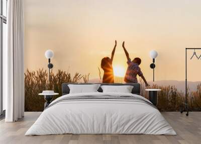 Silhouette of children playing with raised hands on the mountain at the sunset time. Wall mural