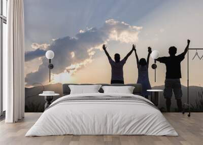 Silhouette of Joyful family stands with raised arms on the mountain at the sunset time. Wall mural