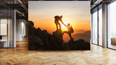 Silhouette Two Male hikers climbing up mountain cliff and one of them giving helping hand. People helping and, team work concept. Wall mural