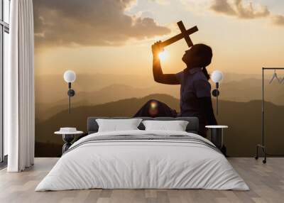 Silhouette young woman praying and holding Christian cross for worshipping God on mountain at sunrise background. Christian, Christianity, Religion copy space background Wall mural