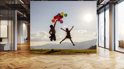 Two children jumping playing with colored balloons at sunset. Wall mural