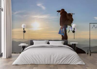 Young man with backpack enjoying sunset on binoculars peak of mountain layers line.Travel hiking. Wall mural