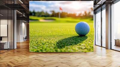 A close-up of a golf ball on a green course with a flag in the background. Wall mural