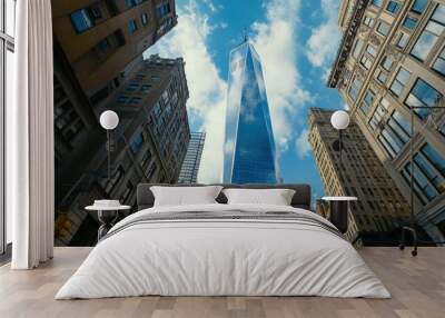 A tall skyscraper rises between historic buildings under a bright blue sky with clouds. Wall mural