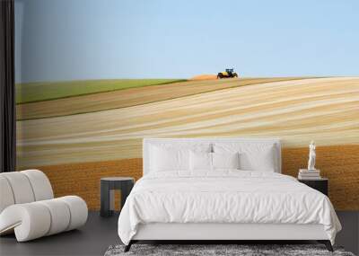 A tractor working on rolling farmland with distinct color patterns under a clear blue sky. Wall mural