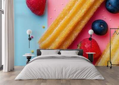 Two fried churros dusted with sugar and surrounded by blueberries, strawberries, and orange slices on a pink and blue background. Wall mural