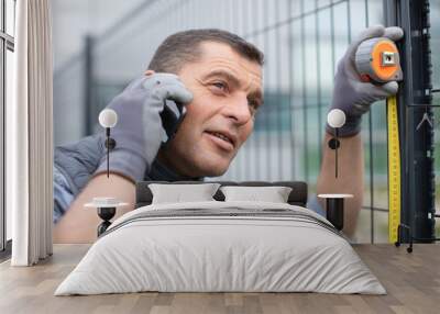 handy man measuring metal fence while calling on phone Wall mural