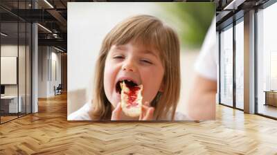 Little girl eating bread with jam on it Wall mural