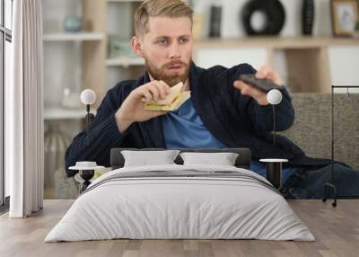 man changing tv channel with remote control while eating sandwich Wall mural