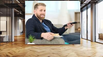 man changing tv channel with remote control while eating sandwich Wall mural