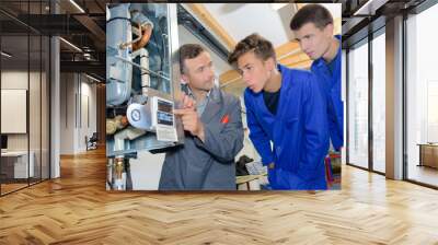 man looking at digital display on boiler with two apprentices Wall mural