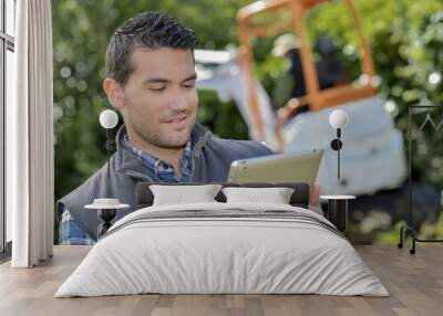 Man looking at tablet, digger working in background Wall mural