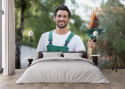 portrait of young man holding rake smiling Wall mural