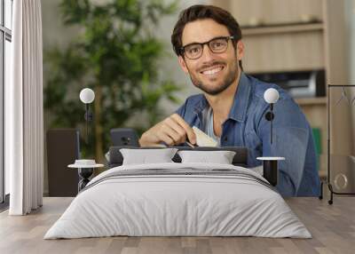 smiling man sitting in office and pays by credit card Wall mural