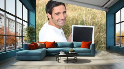 smiling man sitting on the grass with a laptop computer Wall mural