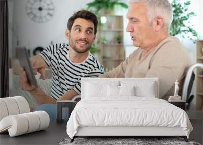 smiling man taking care about his eldery father in wheelchair Wall mural