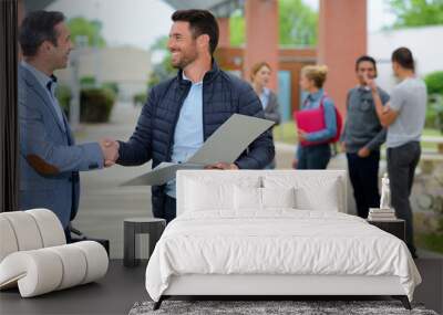 two mature men shaking hands on campus students in background Wall mural