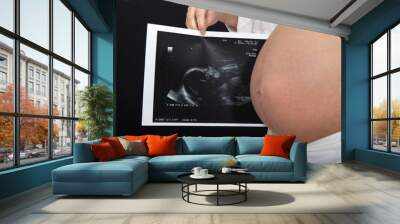 woman holding an obstetric sonogram next to her belly Wall mural